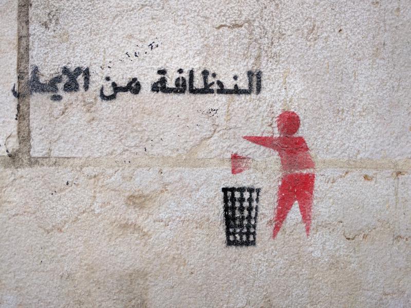 Graffiti with Arabic inscription depicting someone putting trash in a trash can