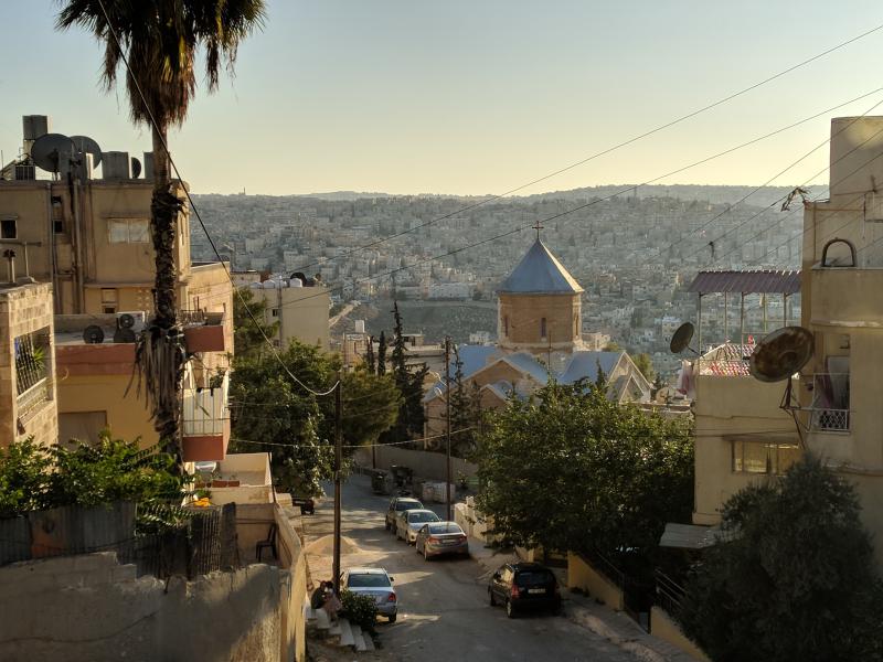 Church in typical Armenian style with pointy blue roof and the city behind it.